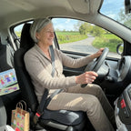Femme de 65 ans au volant, en route chez ses petits-enfants, assise sur le coussin d'assise coccyx gris posé sur le siège conducteur
