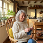 Femme de 65 ans qui tricote dans sa cuisine, calée contre le coussin de chaise épais jaune